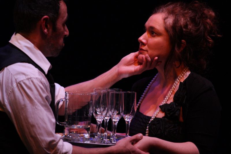 Hedda is carrying a tray of drinks and is confronted by Løvborg, who is stroking her cheek.