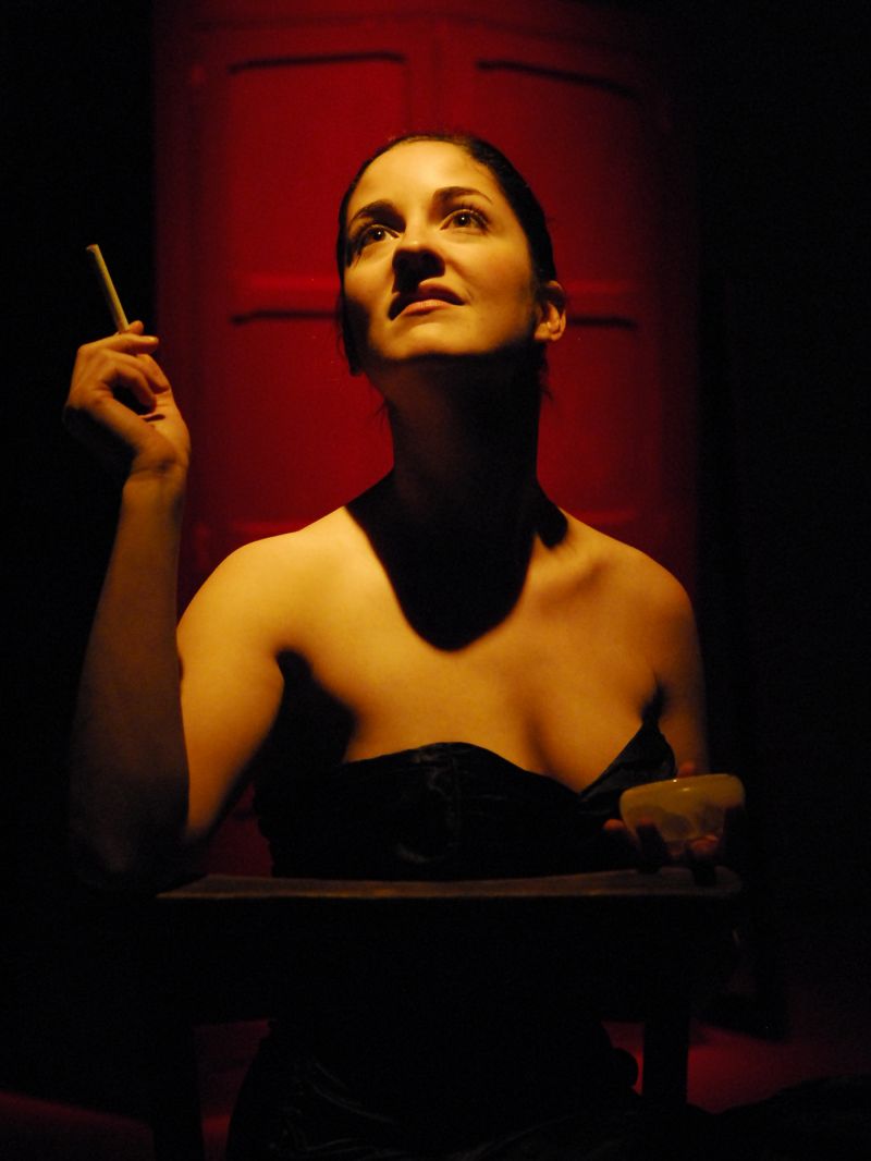 The devil, who takes the shape of an attractive woman in a strapless black dress, is holding a lit cigarette in her left hand looking towards the sky.