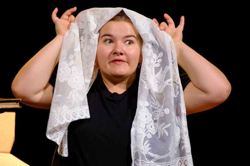 A young girl is looking out from under her wedding veil.